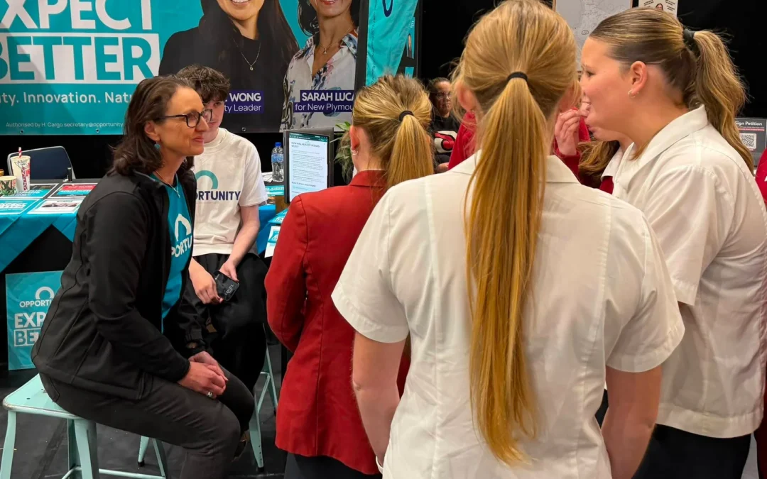 Sarah Lucas speaking with students at the Opportunity campaign stand, beneath a banner featuring Sarah and party leader Qiulae Wong